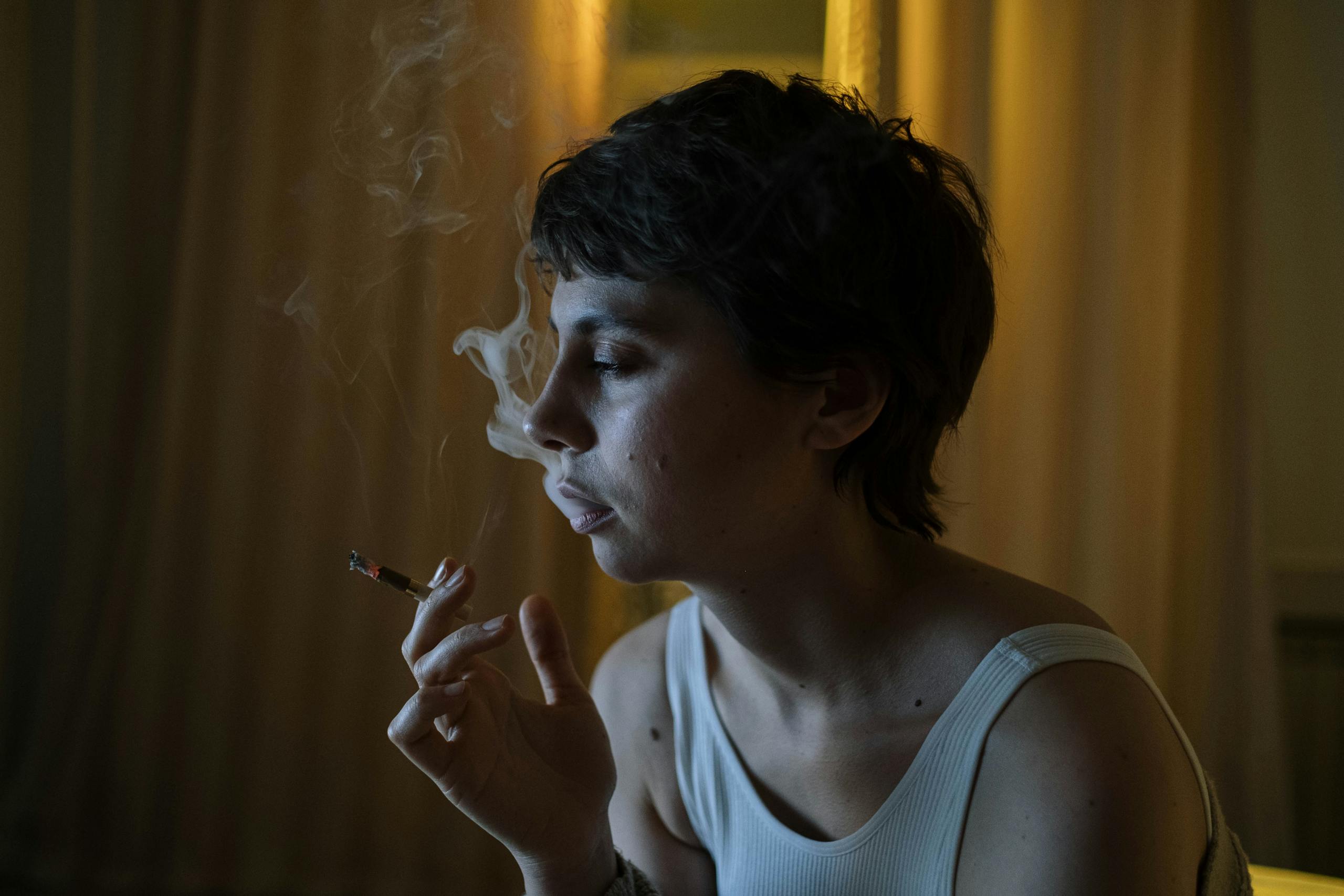 Woman with short hair smoking indoors, reflecting at night, with moody lighting.