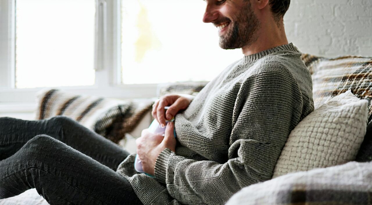 A person covering their stomach with one hand, a hot water bottle beside them, looking relieved