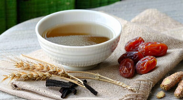 A peaceful scene with a bowl of Ganmai Dazao soup and the herbs licorice, wheat, and jujube.