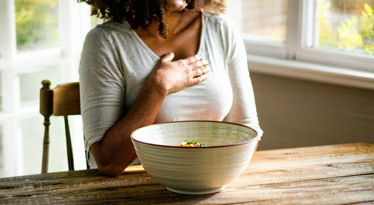 A person holding their abdomen with untouched food in front, showing common discomfort associated with middle jiao deficiency cold