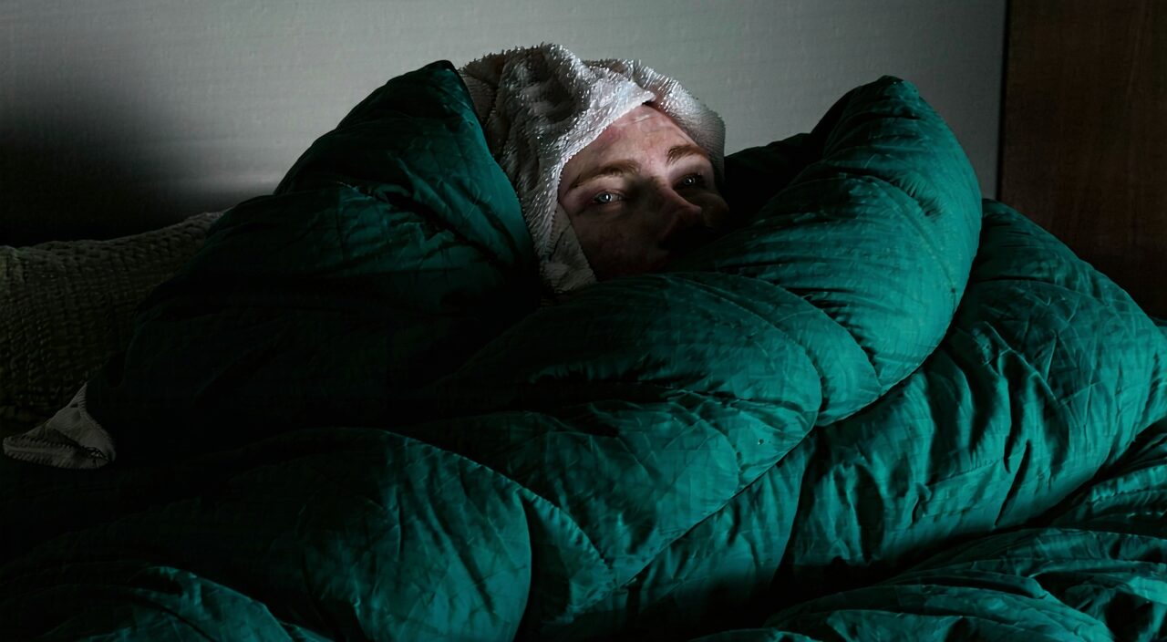 A person lying in bed, tightly wrapped in a thick quilt, with signs of fever on the face and a damp towel on the forehead, the bedroom light quiet and soft, expressing the sick state of wind-cold exterior excess without sweat accompanied by wheezing.