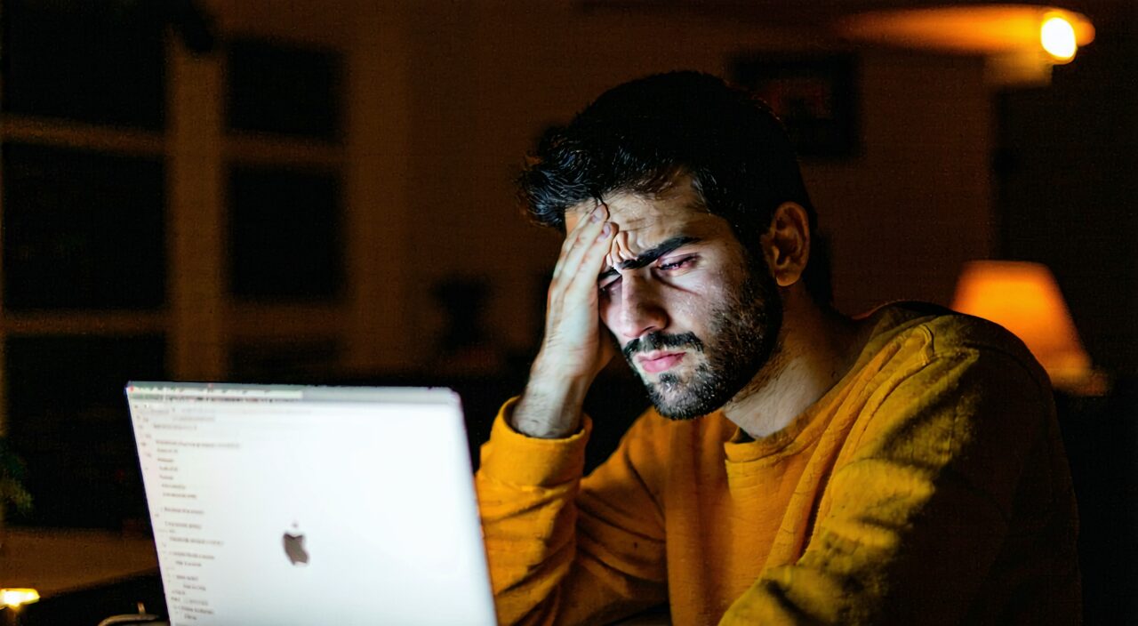 A person working on a computer at night rubbing their eyes, indicating chronic eye fatigue