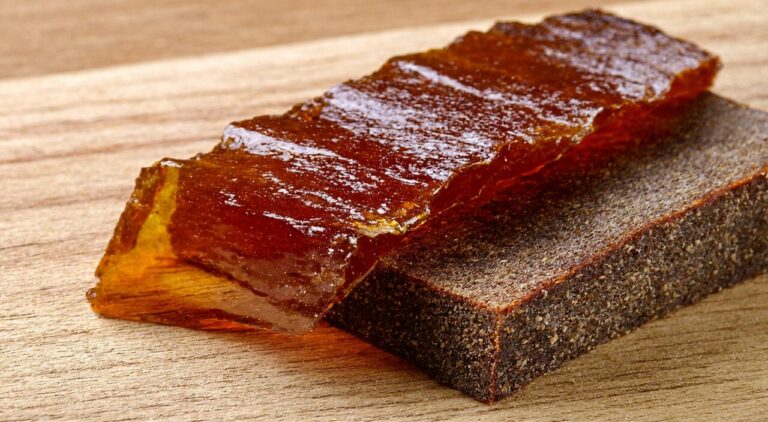 A close-up of a group of honey-fried licorice slices with glossy reddish-brown surfaces; one slice is gently bent, revealing the cross-sectional texture.