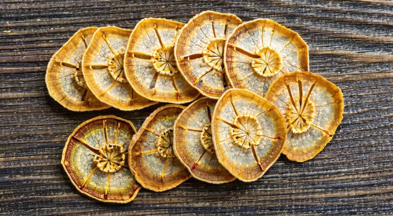 Dried hemispherical slices of bitter orange with yellowish-brown peel and oil dots, placed on a wood-grain table surface.